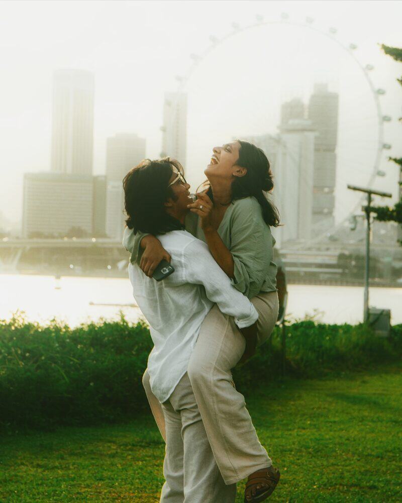 Samesh lifting Raghvi, both laughing, by the water with a ferris wheel behind